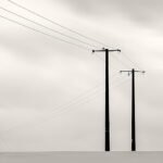 Black and white photograph by Bernard Donjean that shows two electric poles in a snowy meadow (name of the photograph : Two Electric Poles)