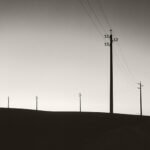 Black and white photograph by Bernard Donjean that shows five electric poles photographied against the light (name of the photograph : Following the Leader)