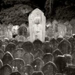 Black and white photograph by Bernard Donjean that shows a tall Jizo statue in the middle of many engraved stones (name of the photograph : Sculpted Stones and Jizo)