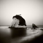 Black and white photograph by Bernard Donjean that shows a rock formation emerging from the surface of the sea (name of the photograph : Suzumeshima Rock)