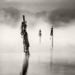 Black and white photograph by Bernard Donjean that shows three submerged masts carrying folded ropes (name of the photograph : Strange Figures)