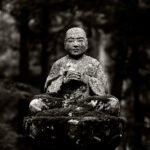 Black and white photograph by Bernard Donjean that shows a small Buddha statue praying on a grave in Okuno-In (name of the photograph : Spiritual Thoughts)