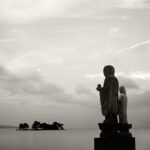 Black and white photograph by Bernard Donjean that shows two statues of jizo face to the lake Shinji (name of the photograph : Sodeshi and Lime Jizos)