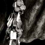 Black and white photograph by Bernard Donjean that shows small strap-style sandal charms attached to the feet of a statue of a traveling monk (name of the photograph : Straw Sandal Charms)