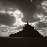 Black and white photograph by Bernard Donjean that shows the shape of Mont-Saint-Michel under a broken clouds sky (name of the photograph : Broken Clouds)