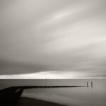 Black and white photograph by Bernard Donjean that shows a immersed wave breaker and a ship approaching on the horizon : Approaching Ship)