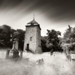 Black and white photograph by Bernard Donjean that shows the Saint-Martin tower, located in Comblain-au-Pont, and the old cemetery around it (name of the photograph : Saint-Martin Tower and Cemetery)