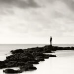 Black and white photograph by Bernard Donjean that show a statue of a contemplator installed on a water breaker (name of the photograph : The Contemplator)