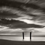 Black and white photograph by Bernard Donjean that shows two isolated stakes on a beach (name of the photograph : Isolated Stakes)