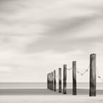 Black and white photograph by Bernard Donjean that shows a a lign of roped wooden poles which mark the limit of the swimming beach area (name of the photograph : Kite Bird Scarer)