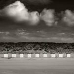 Black and white photograph by Bernard Donjean that shows nine aligned beach huts on the beach of Nieuwesluis in Zeeland (name of the photograph : Beach Huts Alignment)