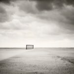 Black and white photograph by Bernard Donjean that shows a lone fence located at the end of a concrete path on the beach of Knokke-Heist (name of the photograph : End Fence)